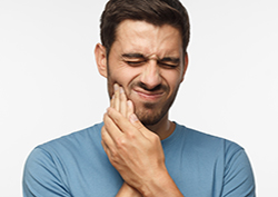 Young male with his face distorted in pain, hands pressed to cheek as he is experiencing severe toothache or tooth pain