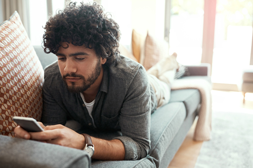 Shot of a handsome young man using his cellphone while relaxing on the couch at home