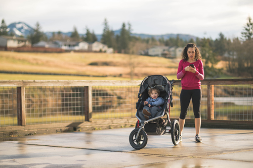 Young Hawaiian mom on cell phone next to young boy in stroller.